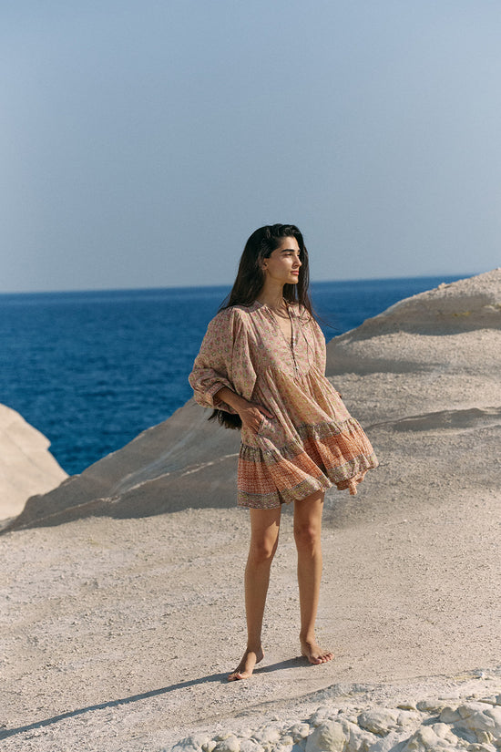 Full-length view of woman on white coastal rock by deep blue sea wearing the Daughters of India Bhoomi Mini Dress in Sunset, showing the complete boho silhouette