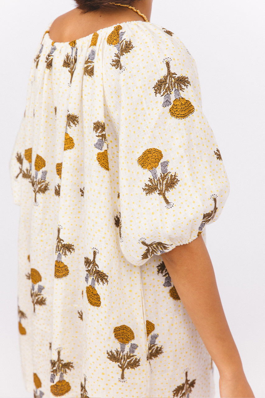 Dahlia Mini Dress Marigold — close-up shoulder and sleeve detail, off-shoulder neckline, billowy puff sleeve, white linen with amber marigold botanical hand block print, Jaipur artisan crafted | Daughters of India