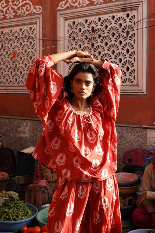 Ria Blouse Ruby Red — lifestyle Indian market portrait, model wearing ruby red hand block print cotton blouse among colourful bazaar produce and spices, artisan Jaipur India | Daughters of India