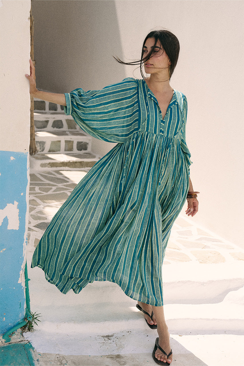Woman standing on a white staircase wearing the Daughters of India Kyra Maxi Dress in Spearmint with the fabric billowing in the breeze, Greek island backdrop